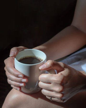 Close up of Comforting cozy female hands holding a coffee glass with the morning sunlight that...