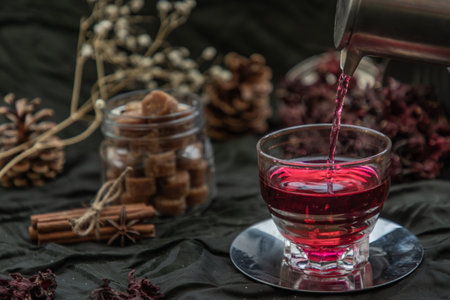 Roselle tea (Jamaica sorrel, Rozelle or hibiscus sabdariffa ) is poured from a kettle into glass cup  with dry roselle and brown cane sugar cube. Healthy herbal tea rich in vitamin C and minerals. The concept of health. Organic and Summer drink, Drinks & Beverages, Selective Focus.の写真素材