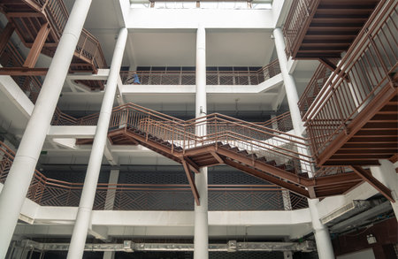 Bangkok, Thailand - 01 Jan, 2528 - the interior of the Building at Wongwian Yai. The building's design features a contemporary architectural style with a complex arrangement of crisscrossing steel staircases and railings connecting multiple levels, all within an open floor plan. use as Wallpaper, Poster and Space for text, Selective focus.の写真素材