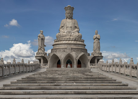 Bangkok, Thailand - 18 Oct, 2025 - A large white marble statue of Guanyin of the Goddess of Mercy. It is seated on a celestial platform and is surrounded by smaller statues against a clear blue sky at the Guanyin Bodhisattva's Hall in Bangkok, Selective focus.の写真素材