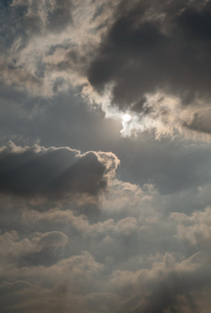 A dramatic cloudscape unfolds, with dark, heavy clouds as bright sunlight pierces through them....