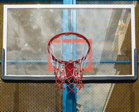 An orange metal basketball rim and net are mounted on a fiberglass backboard, prominently framed by...