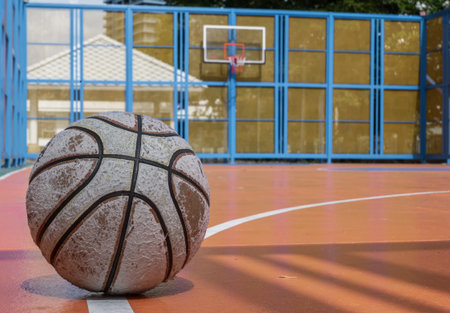 On the orange outdoor basketball court, a tired basketball waits. Space for text.の写真素材
