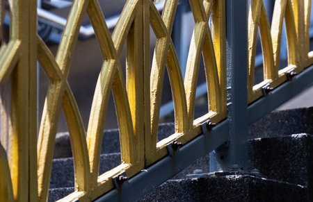 Bangkok, Thailand - Mar 02, 2025 - A lattice of interlocking arches, finished in a luminous gold, serves as the centerpiece of this industrial composition. The interplay of light and shadow articulates every bolt and curve, grounding the ornate design within its sturdy gray scaffolding. Below, the textured concrete base absorbs the dark, geometric shadows, punctuating the contrast between delicate craftsmanship and raw material.の写真素材