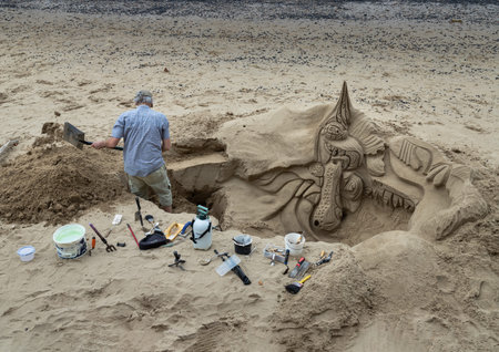 London, UK - Aug 18, 2025 - a sand artist at working on a detailed sand sculpture on a small beach,...