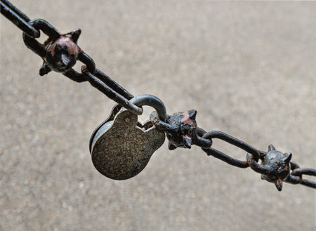 A weathered, vintage-style padlock serves as the central link in a heavy spiked chain. This...