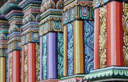 Bangkok, Thailand - Jan 02, 2023 - A side-angle view of the square, polychromatic pillars at the Sri Maha Mariamman Temple, showcasing a vibrant mastery of Hindu architecture. Each pillar is a tiered stack of elaborate relief carvings floral scrolls, geometric motifs, and intricate patterns brought to life in a palette of terracotta, lavender, and emerald. Gilded accents weave through the bright hues, adding a regal finish to the rich, textured columns.の写真素材
