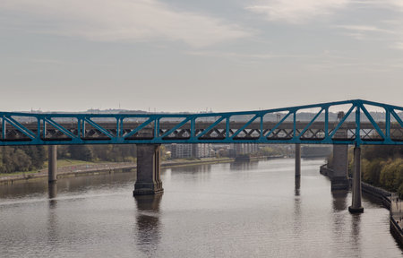 Newcastle, UK - Apr 11, 2025 - The Queen Elizabeth II Metro Bridge spans the Tyne as a vibrant, cobalt-blue ribbon of steel, its geometric trusses etching a modern rhythm against a muted sky. Supported by formidable concrete piers, the structure arches ovのeditorial素材