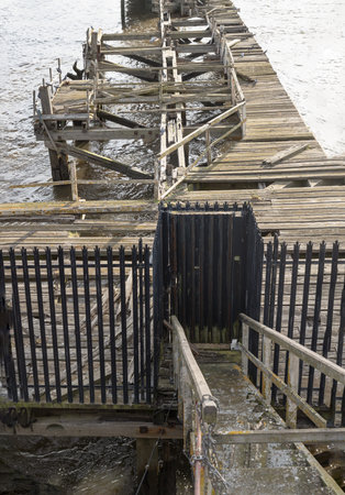 Newcastle, UK - Apr 11, 2025 - A broken of wooden supports of old timber jetty next to Swing bridge or Swing span bridge spanning the River Tyne. Crumbling pier over river, use it as your Wallpaper, Poster and Space for text, Selective focus.のeditorial素材