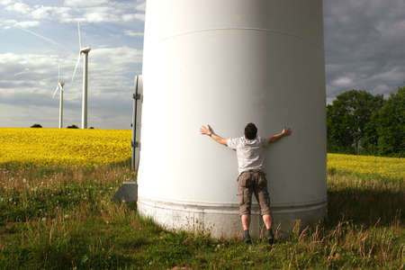 Man embraces a Windmill in front of a rape fieldの写真素材
