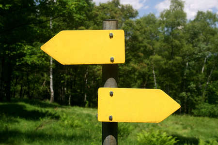 Two yellow arrow signs, one right, one left direction in front of treesの写真素材