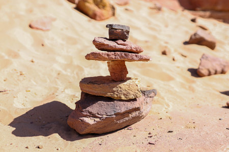 On the sandy surface, a stack of stones is built from red and brown stones of various sizes and shapes, stacked on top of each other. The bottom stone is the largest, while the top one is the smallest.の写真素材