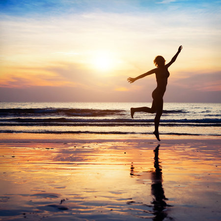woman silhouette jumping on the beach at sunsetの写真素材