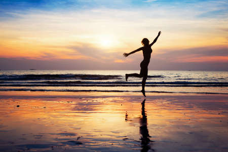 woman silhouette jumping on the beach at sunsetの写真素材
