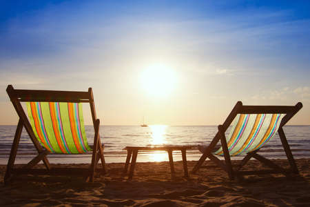 couple of chairs and table on the beach at sunsetの写真素材