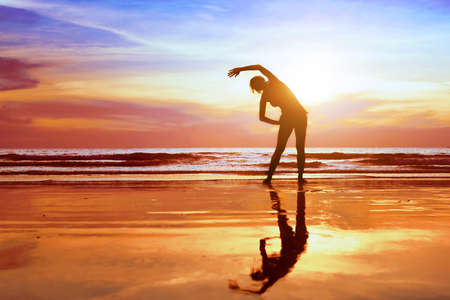 exercise on the beach at sunset, beautiful silhouette of young womanの写真素材