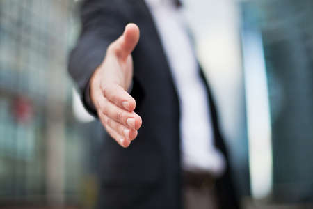 Businessman offering for handshake on office buildings background