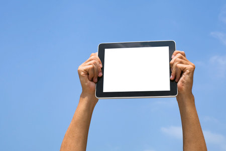 hands holding tablet with blank empty white screen on blue sky background