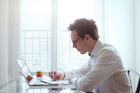 young business man working with documents and laptop in bright office interiorの写真素材