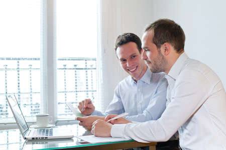 two smiling happy business men working on project in the officeの写真素材