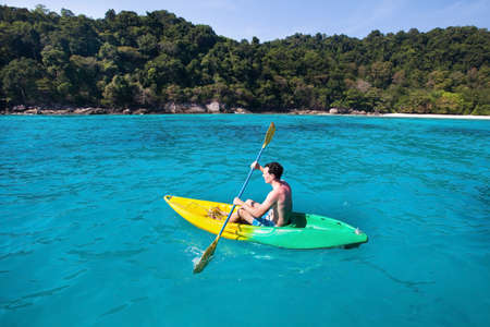 young caucasian man on kayak near paradise island in turquoise waterの写真素材
