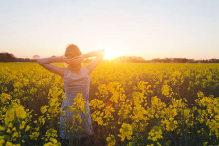young woman enjoying summer and nature in yellow flower field at sunset, harmony and healthy lifestyleの写真素材