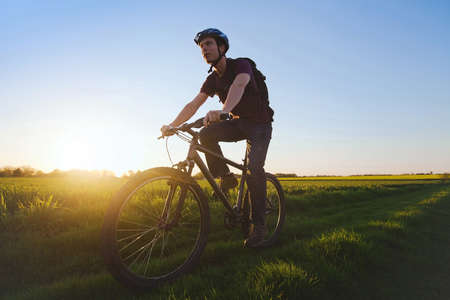 young sportive man riding bicycle outdoors at sunsetの写真素材