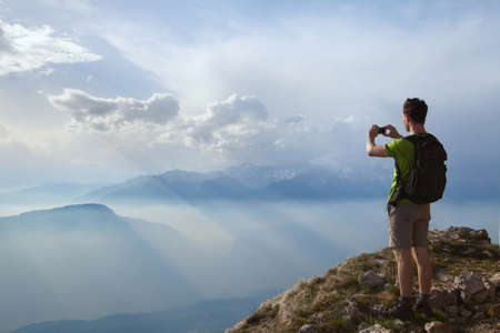 hiker taking photo of beautiful mountain landscape with mobile phoneの写真素材