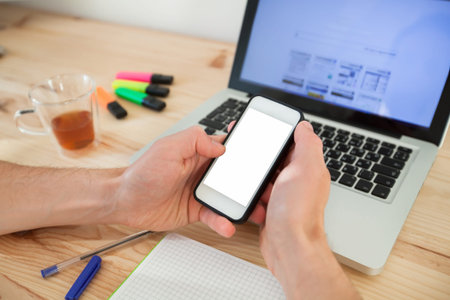 man using smartphone with white screen near laptop in home interiorの写真素材