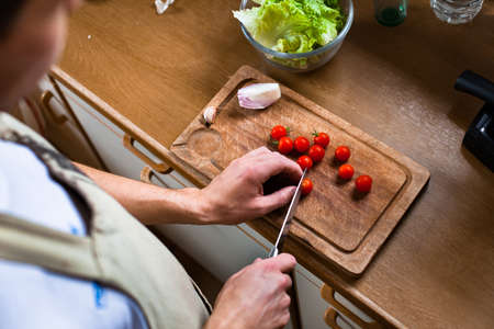 man cooking salad in the kitchen, male hands cutting tomatoes, healthy foodの写真素材