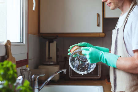 man washing dishes in the kitchen sink at home, close up of hands with sponge and soap, houseworkの写真素材