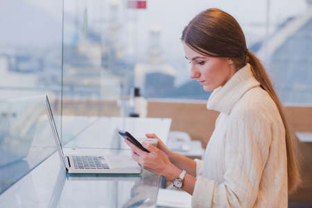 woman using smart phone in modern cafe inerior, mobile application, checking emailの写真素材