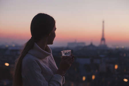 woman enjoying beautiful panoramic view of Paris with cup of coffee, cozy evening in cafeの写真素材