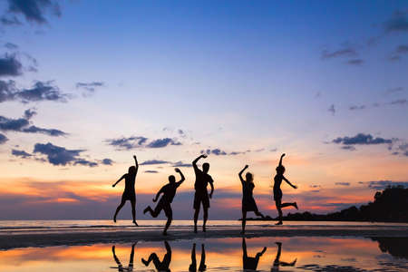 group of people jumping on the beach at sunset, silhouette of friends having fun togetherの写真素材
