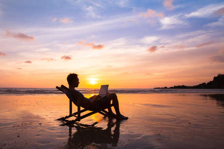 silhouette of happy business man with laptop working on the beach