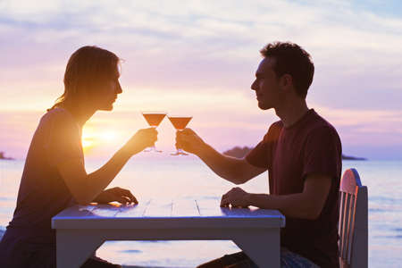 couple in restaurant, drinking cocktails on the beach at sunsetの写真素材