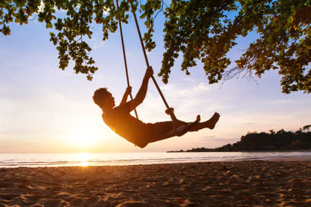 swing on paradise tropical beach at sunset, happy people enjoying summerの写真素材