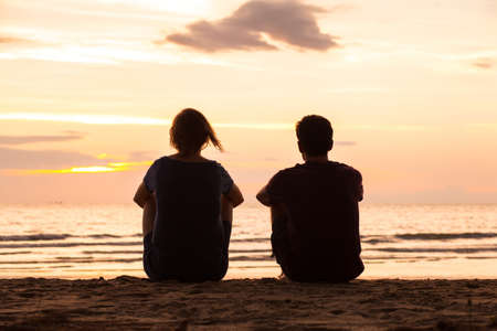 friends sitting together on the beach and watching sunset, friendship conceptの写真素材