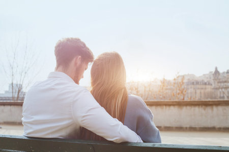 dating or first love, young couple sitting together on the bench, view from the backの写真素材