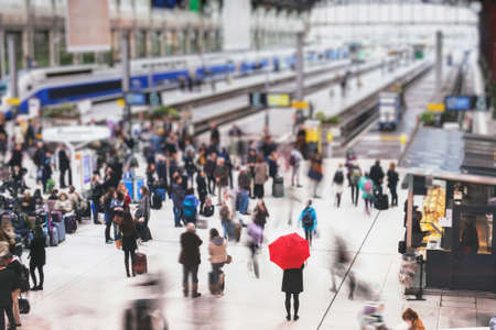 woman with red umbrella waiting at train station and blurred people in motion, solitude conceptの写真素材