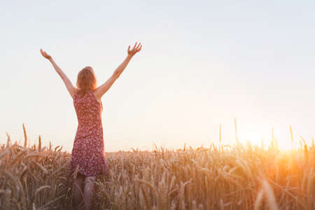 breathing, woman with raised hands enjoying sunset in the fieldの写真素材