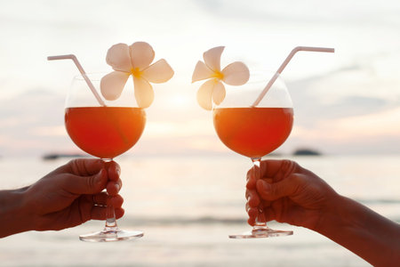 Honeymoon celebration on the beach, couple cheering with tropical cocktails at sunsetの写真素材