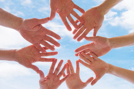 Team or brotherhood concept, group of people putting hands together against blue sky