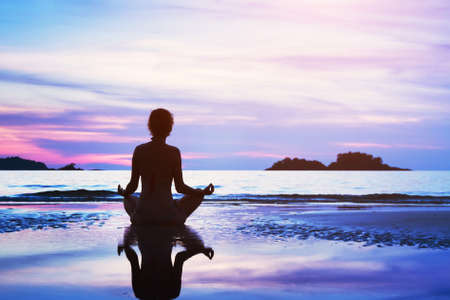 beautiful yoga background, silhouette of woman meditating on the beach at sunsetの写真素材