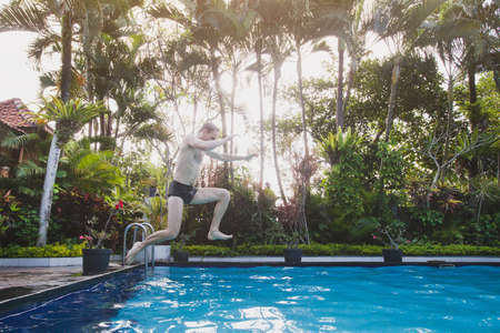 Happy tropical holidays, jumping to the swimming pool in hotelの写真素材