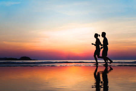 Jogging and healthy lifestyle, two runners silhouettes on the beach at sunset, workout and sportの写真素材