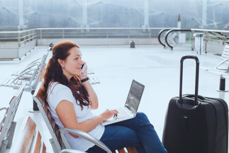 Woman in airport talking by phone and checking emails on laptop, business travel, mobile wifi connectionの写真素材