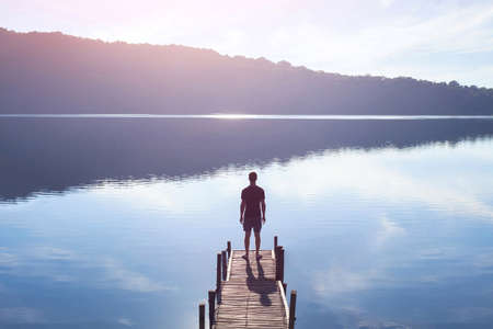 Dreamer, silhouette of man standing on the lake wooden pier at sunset, human strength, psychology concept