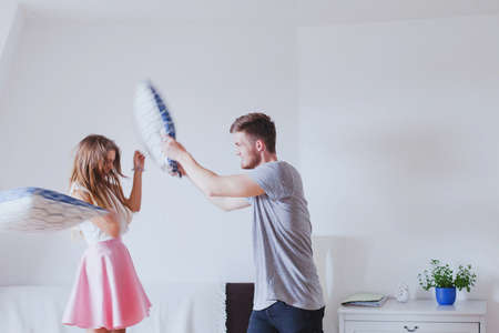 Pillow fight, young happy family couple having fun at home in the morningの写真素材
