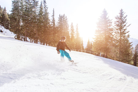 snowboarding in winter Alps, man with fast speed on snowboard in forest slope with backlight